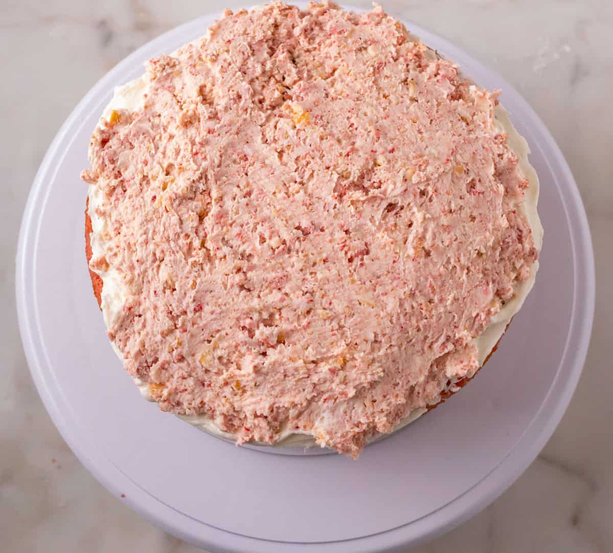 Strawberry Crunch Cake | thewendthousekitchen.com Strawberry crunchy buttercream mixture spread on top of a cake layer.