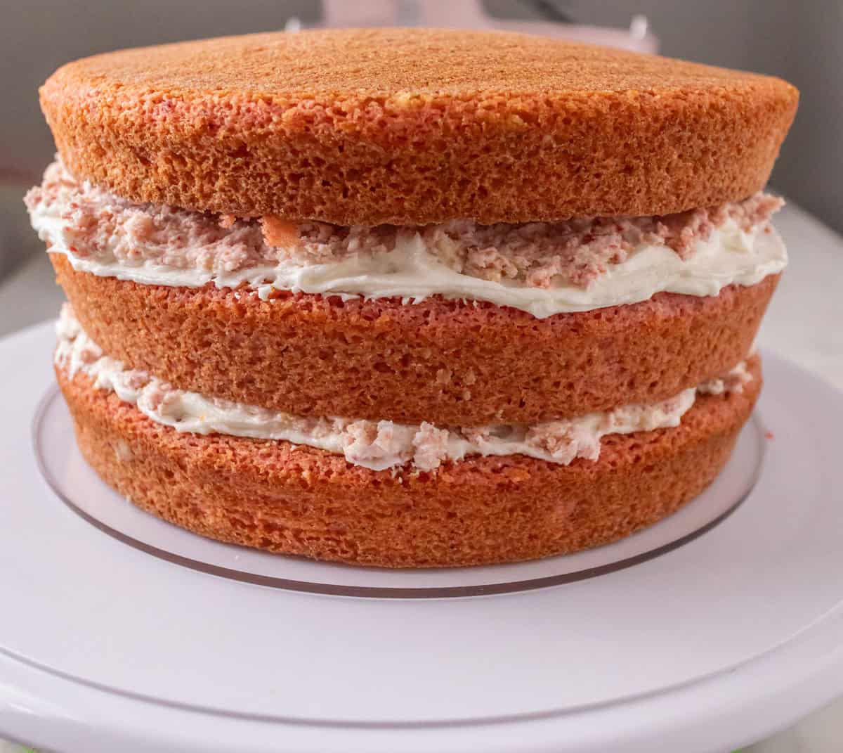 Strawberry Crunch Cake | thewendthousekitchen.com Three strawberry cake layers on an acrylic cake circle. The cake is filled with strawberry crunchy buttercream mixture.