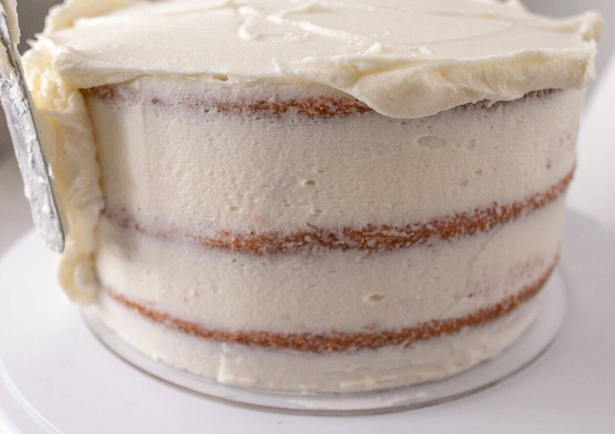 Strawberry Crunch Cake | thewendthousekitchen.com Adding buttercream to the top of a crumb-coated 8-inch, 3-layer cake.