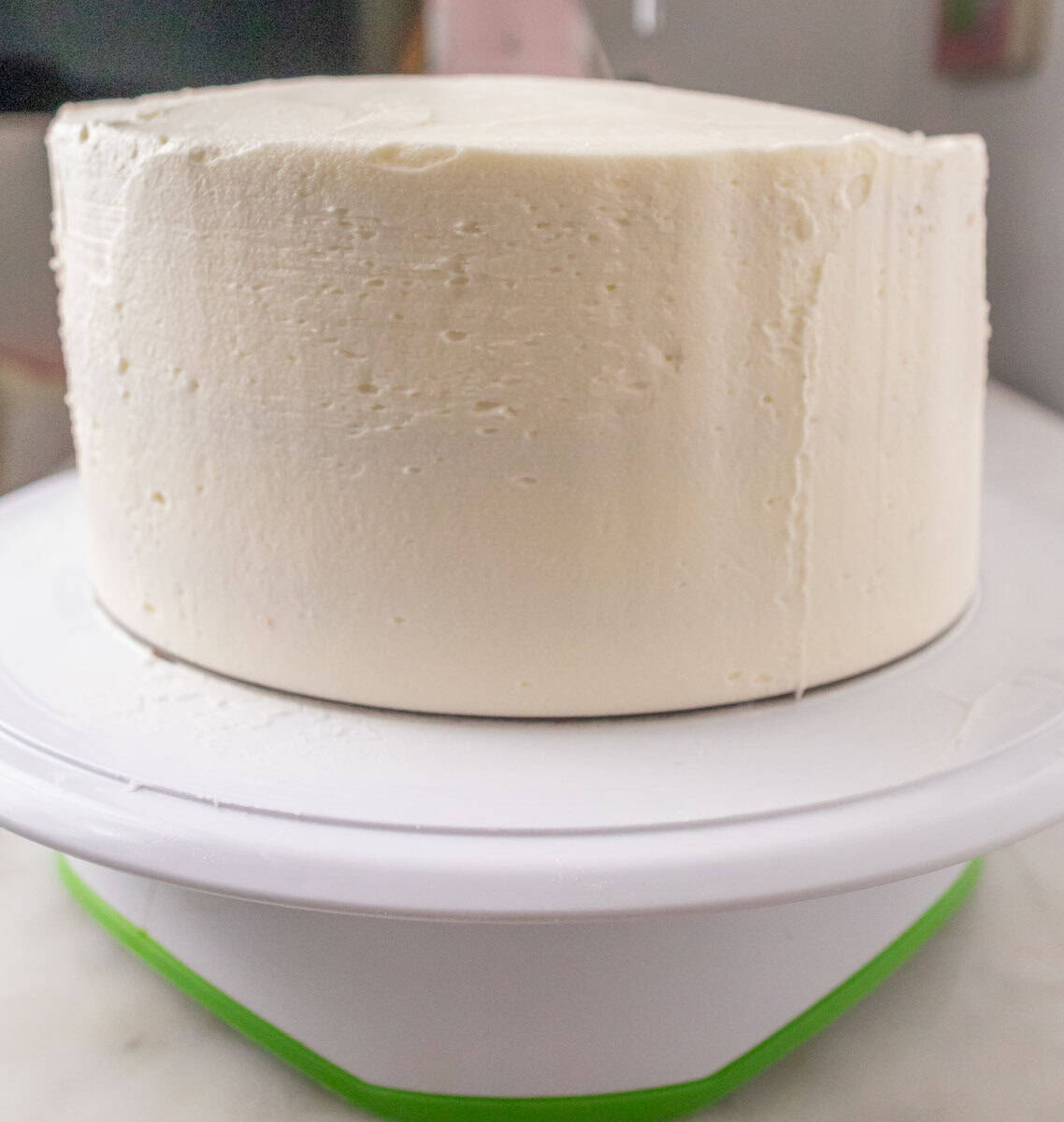 Strawberry Crunch Cake | thewendthousekitchen.com A frosted 8-inch, 3-layer cake with white buttercream on a cake turntable.