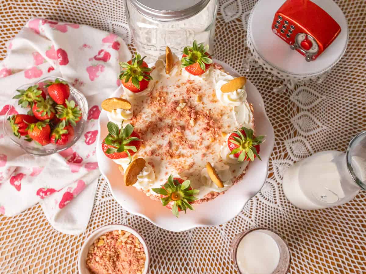 Strawberry Crunch Cake | thewendthouseikitchen.com An overhead shot of a decorated strawberry crunch cake. Strawberries around the cake in a bowl and strawberry crunchies in a small bowl.
