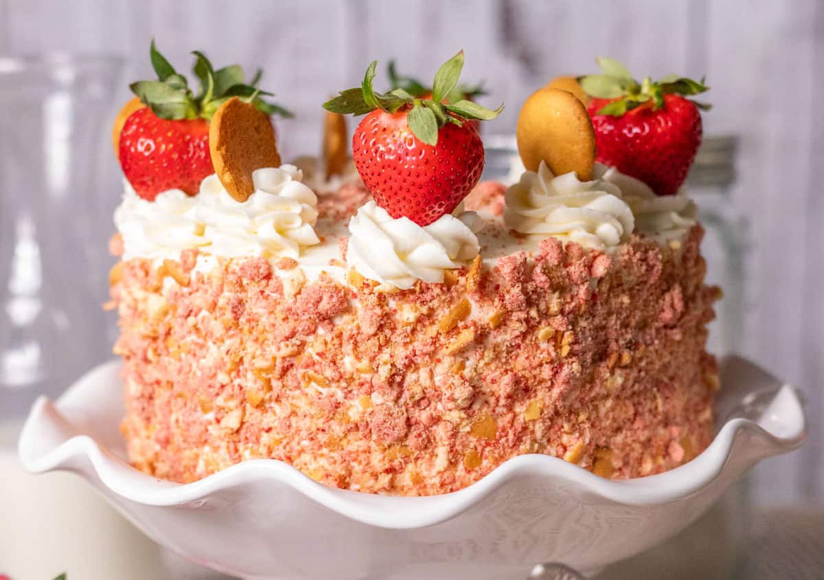 Strawberry Crunch Cake | thewendthousekitchen.com A decorated strawberry crunch cake with fresh strawberries and vanilla wafers on the top with buttercream swirls.